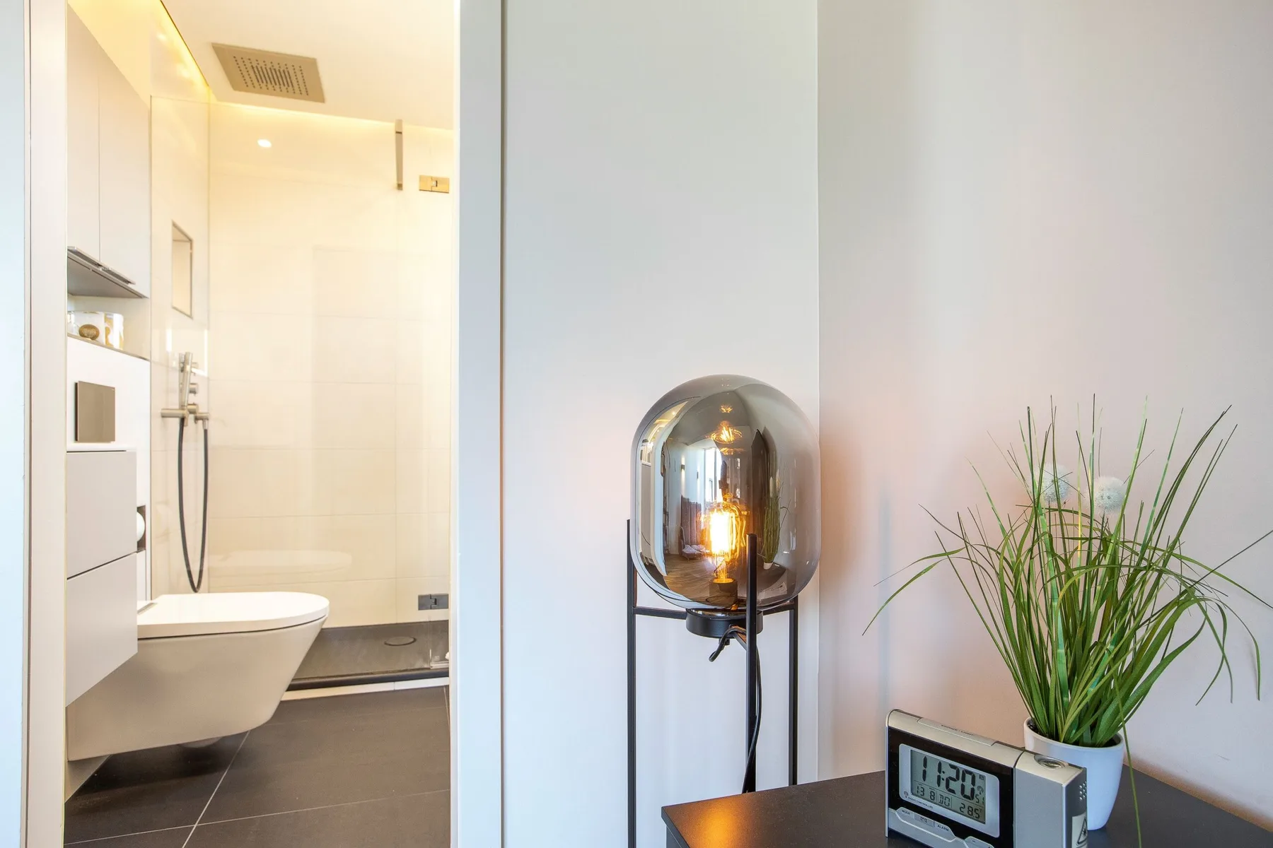 A bathroom with a shower beside a small table and a potted plant.