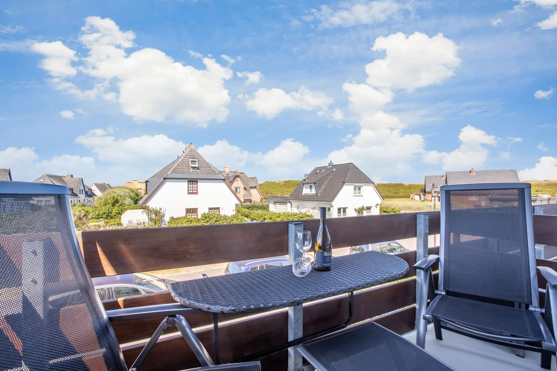A terrace with outdoor seating overlooks houses beneath a partly cloudy sky.