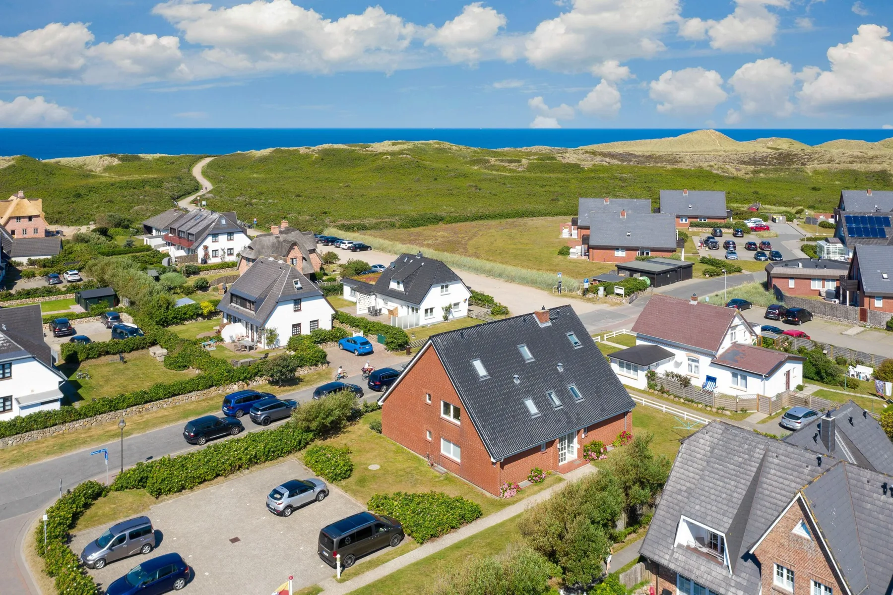 Aerial view of a coastal neighborhood with houses, roads, and the sea beyond.