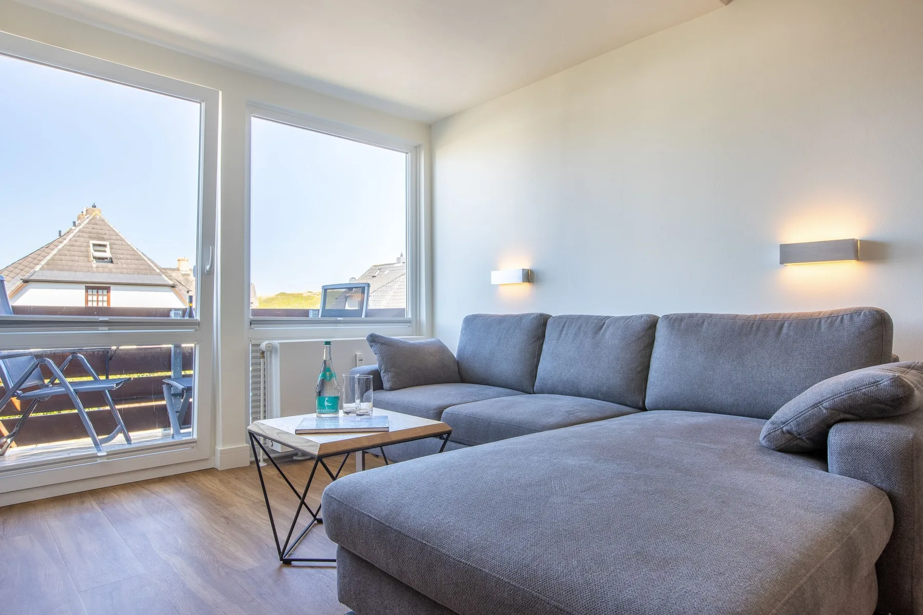A bright living room with a gray sectional sofa beside large windows.