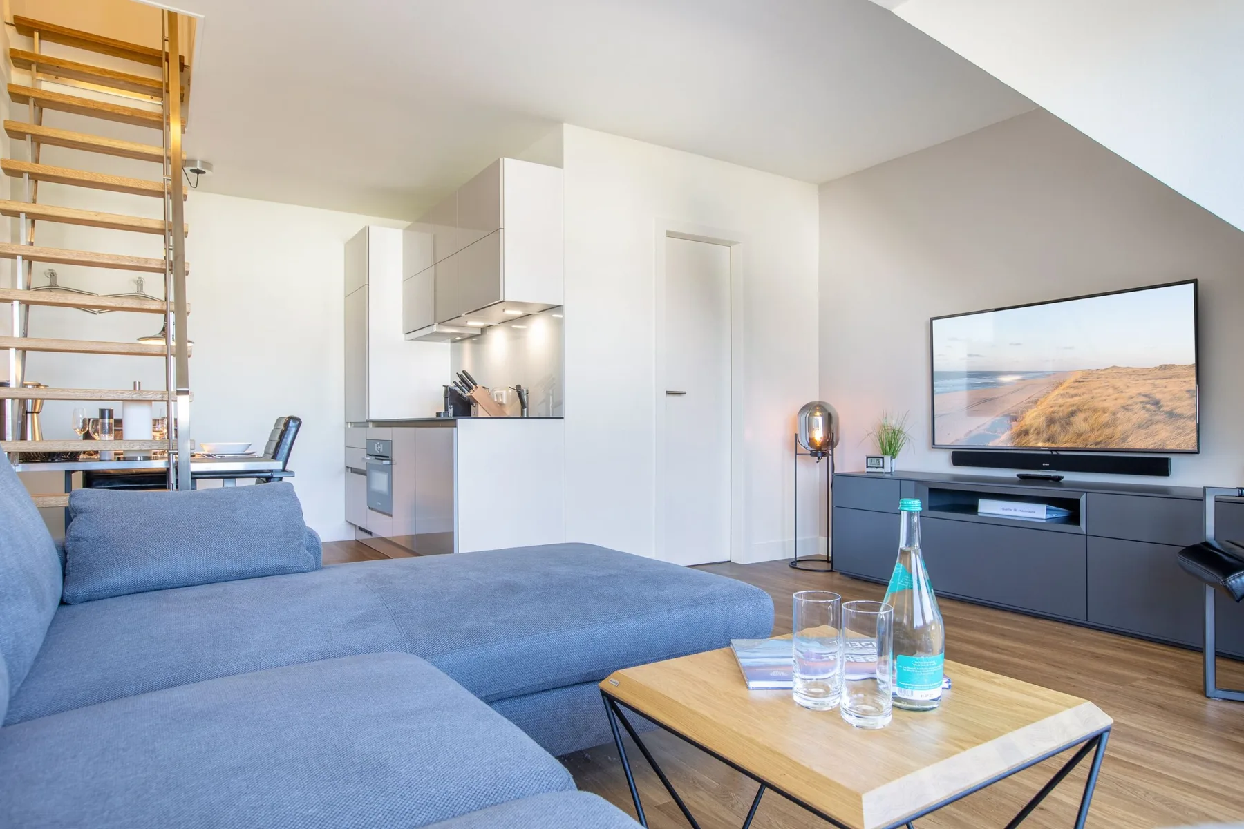 A bright living room with blue seating, a coffee table, and an open kitchen.