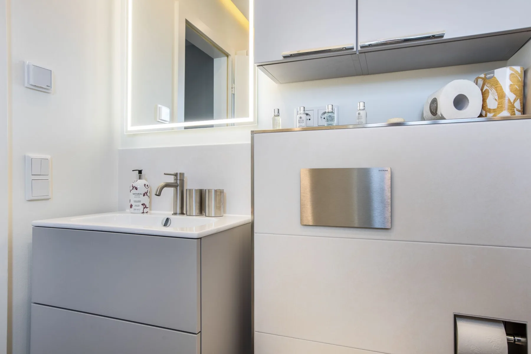 A modern bathroom vanity with a sink, mirror, and wall-mounted storage.