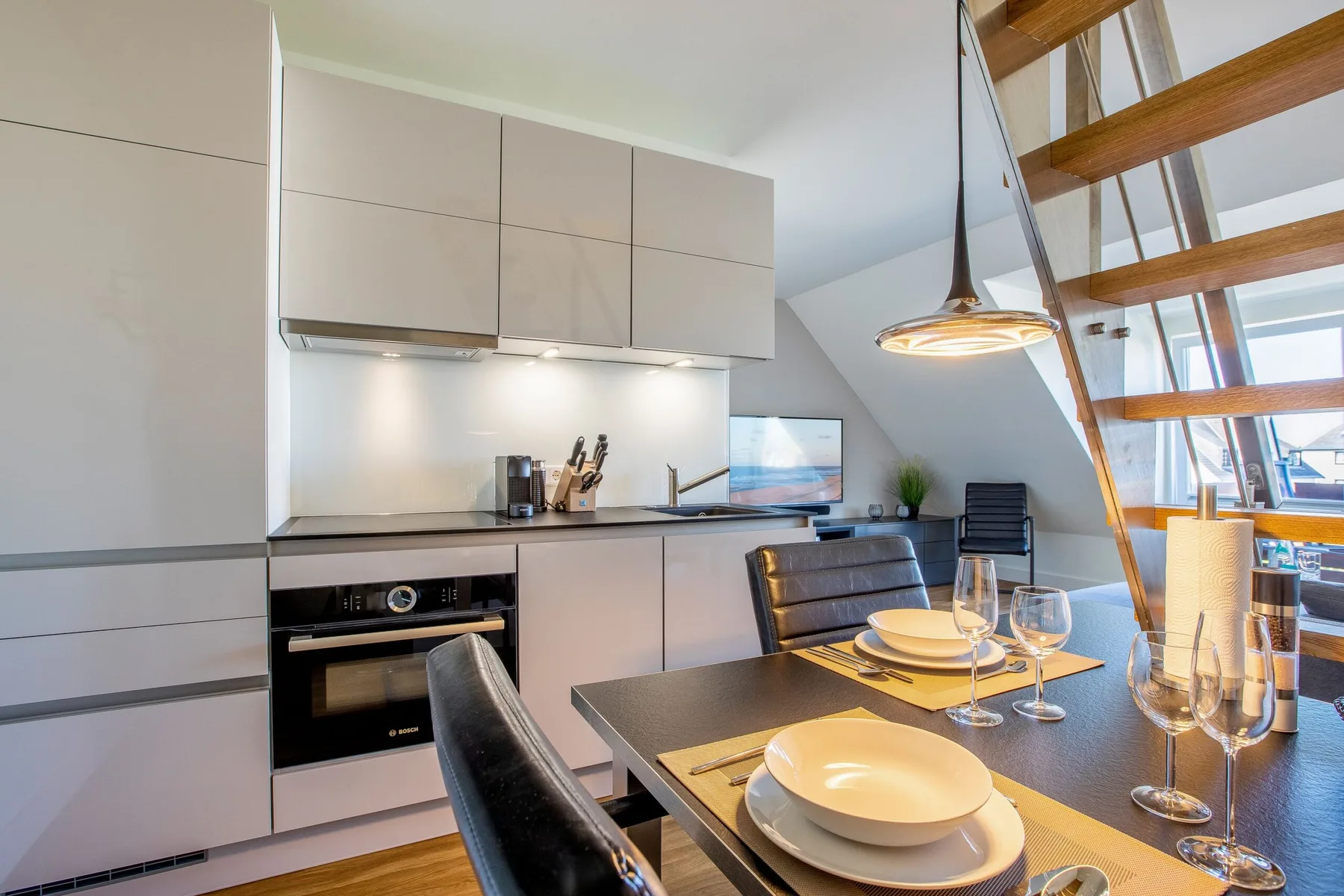A modern kitchen and dining area with a table set beside the staircase.