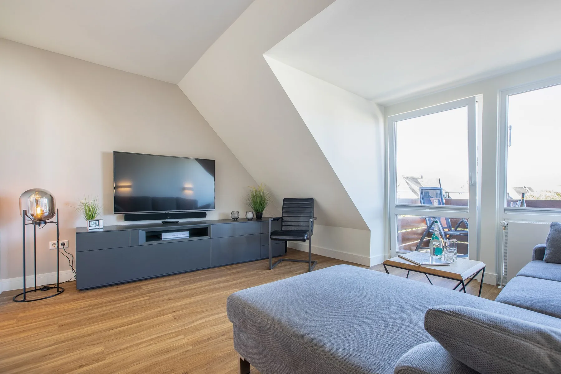A bright living room with a television, seating, and large windows.