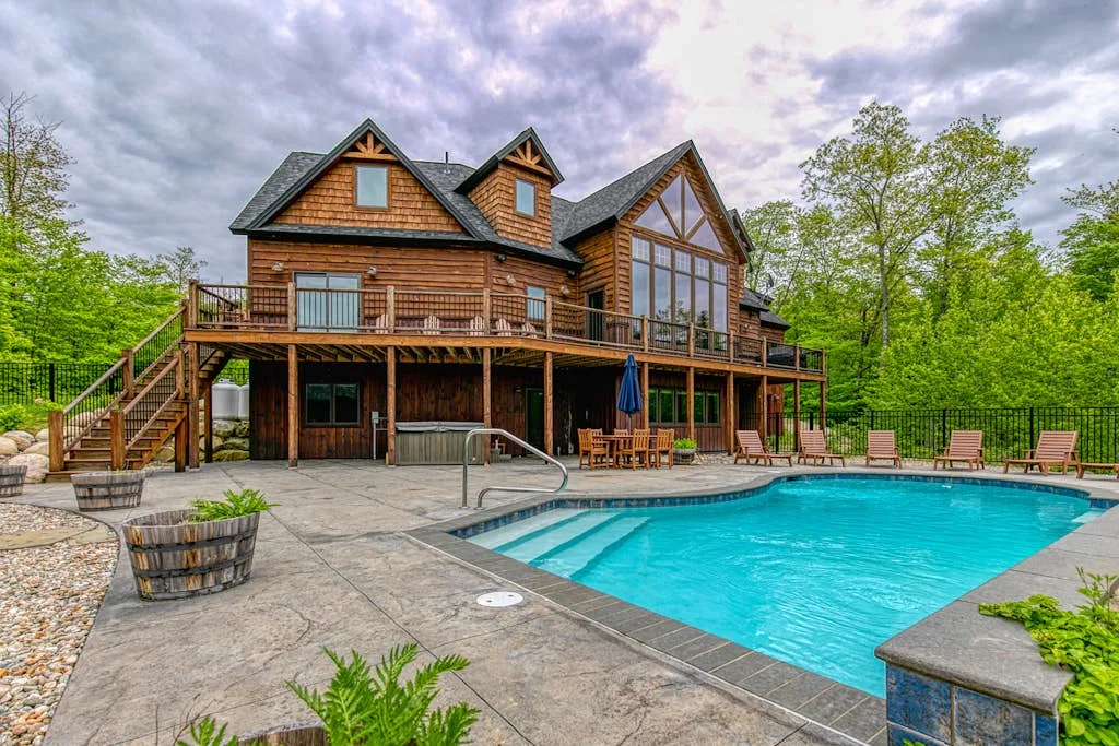 A large house overlooks a swimming pool and paved patio.