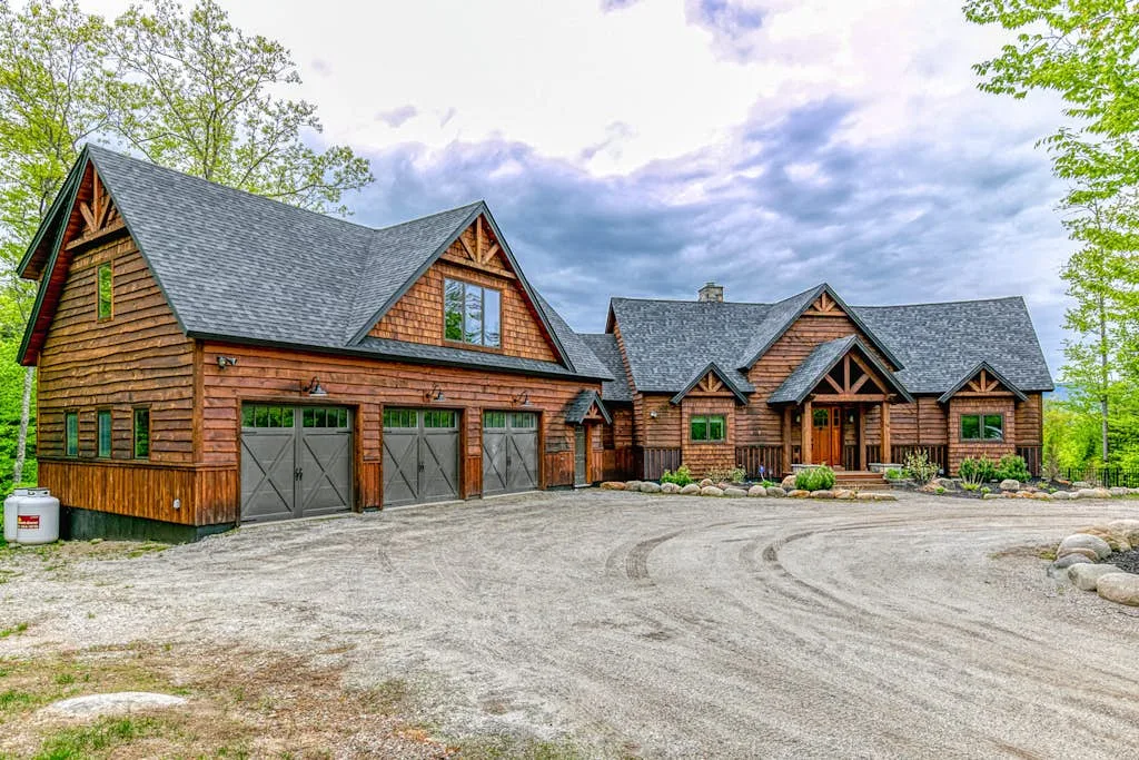 A large timber lodge with several garage doors stands beside a gravel driveway.