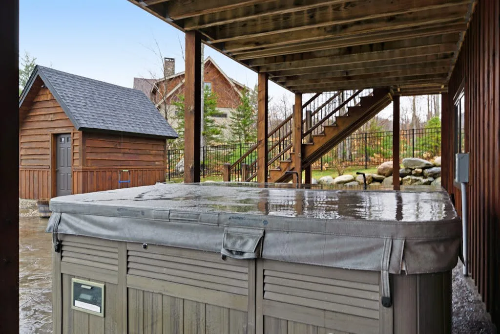 A covered outdoor hot tub sits beside a wooden staircase and small shed.