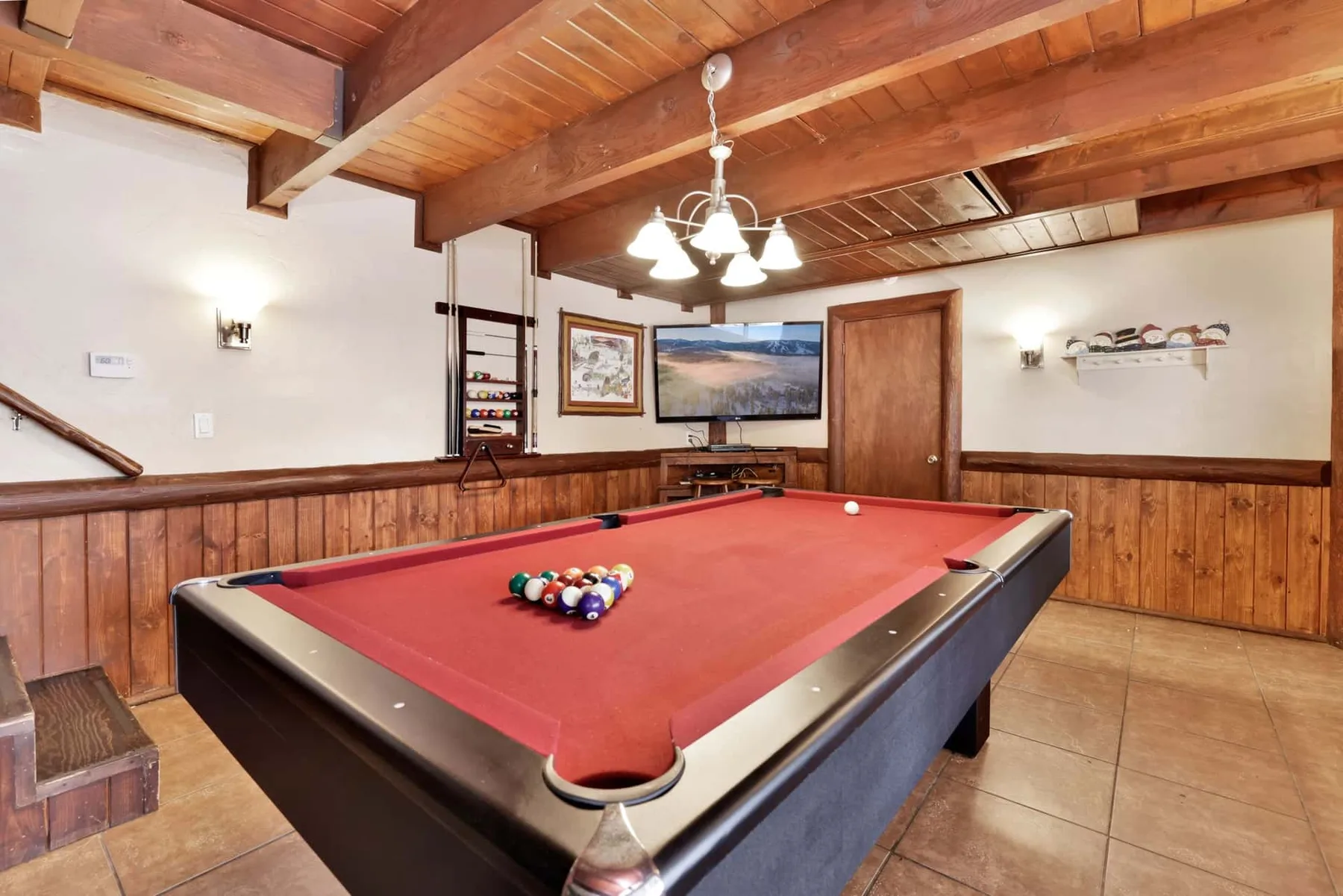 A game room features a red pool table beneath exposed wooden ceiling beams.