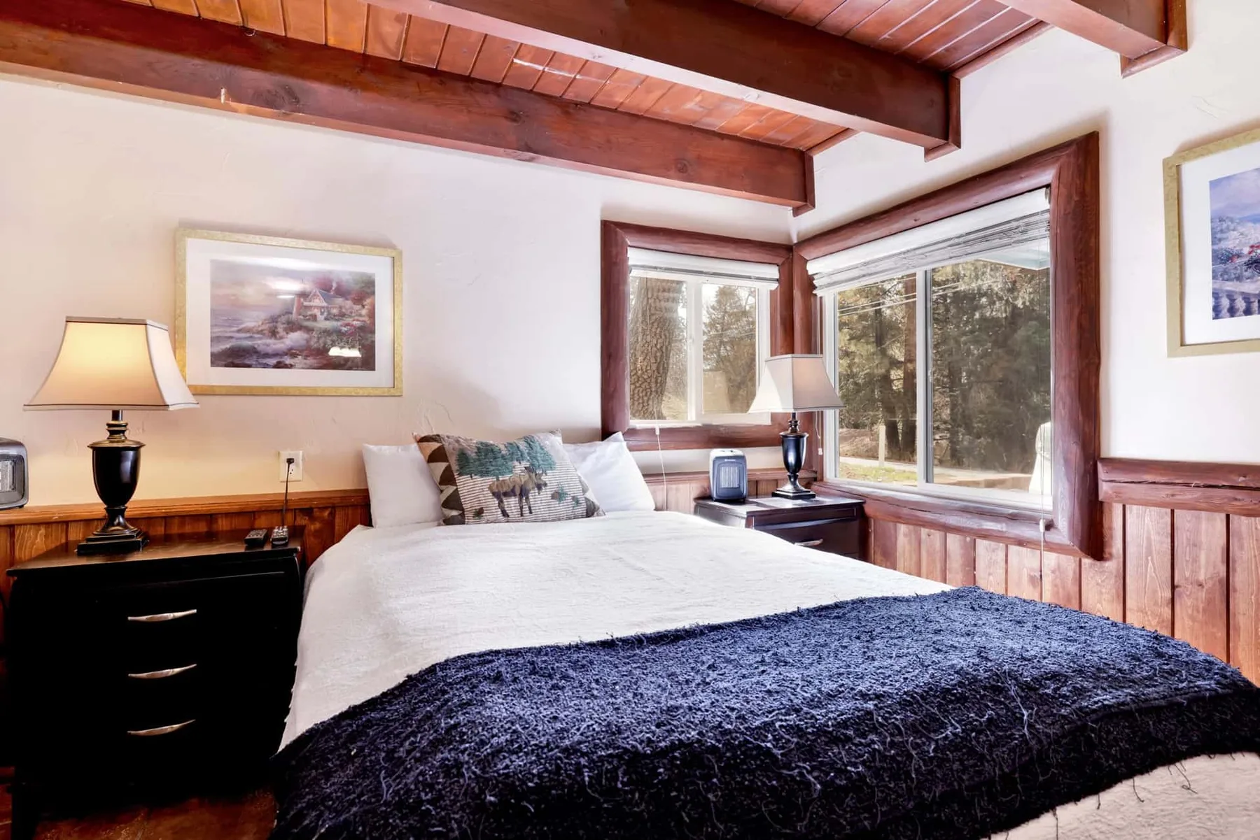 A bedroom with a bed beneath large windows and exposed wooden ceiling beams.