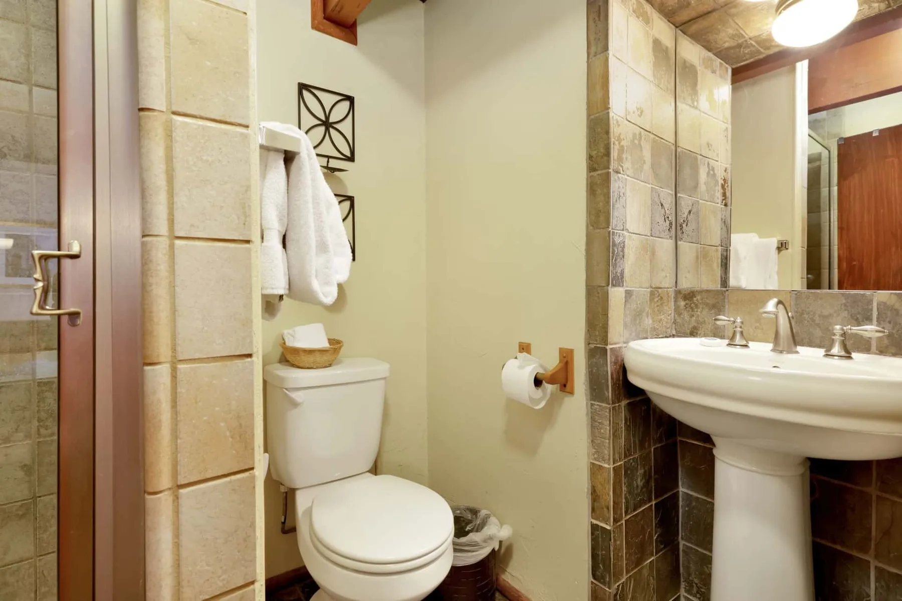 A bathroom with a toilet, pedestal sink, and tiled walls.