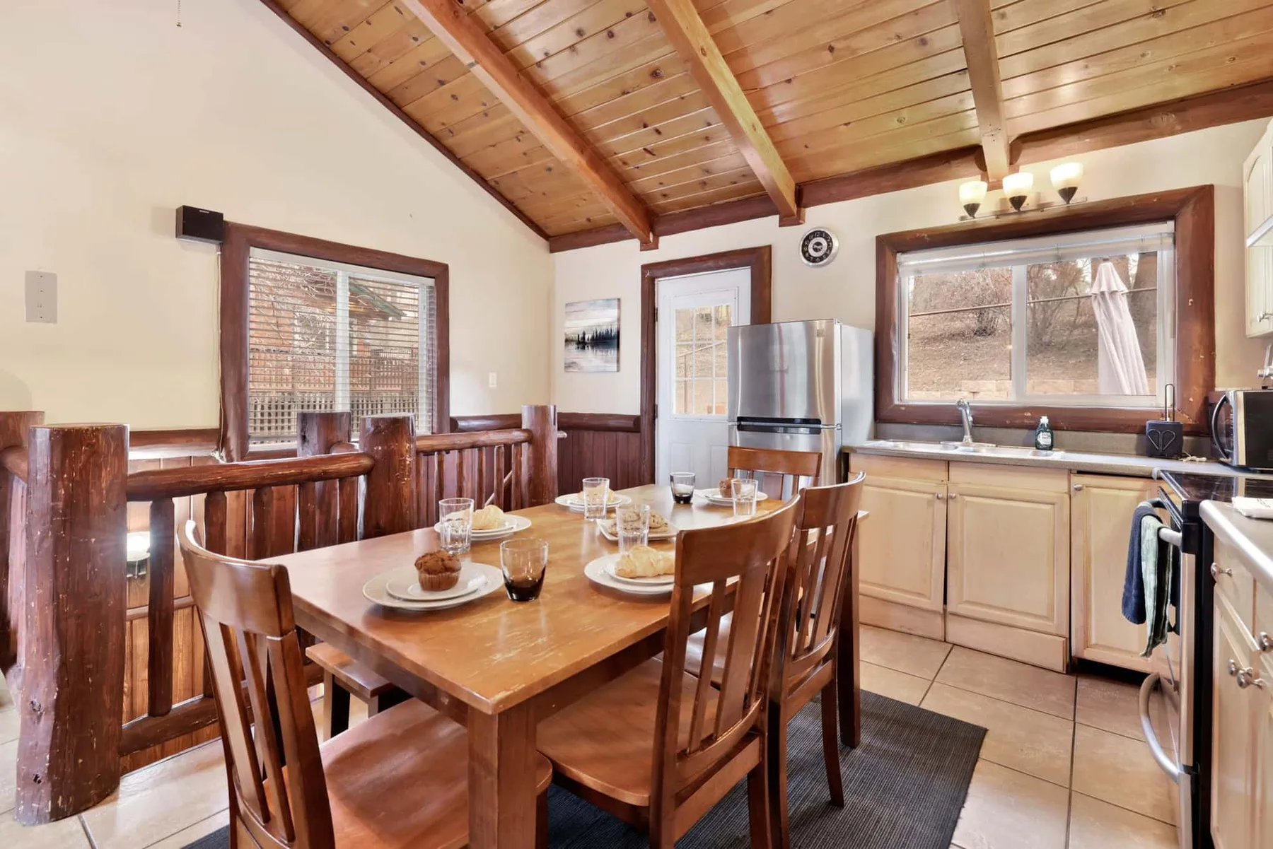 A dining area beside a kitchen, with a wooden table beneath a vaulted ceiling.