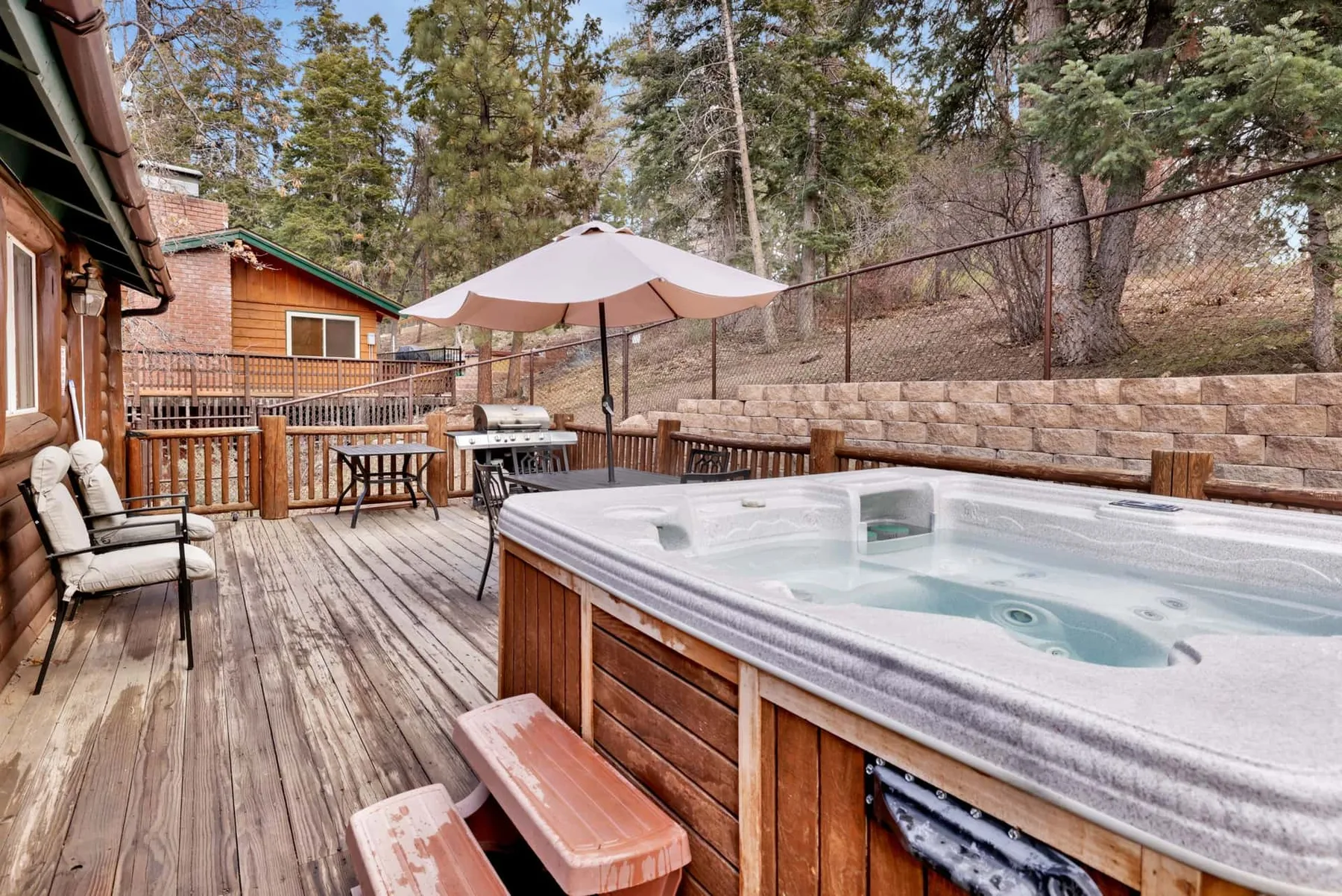An outdoor hot tub sits on a wooden deck beside a shaded seating area.