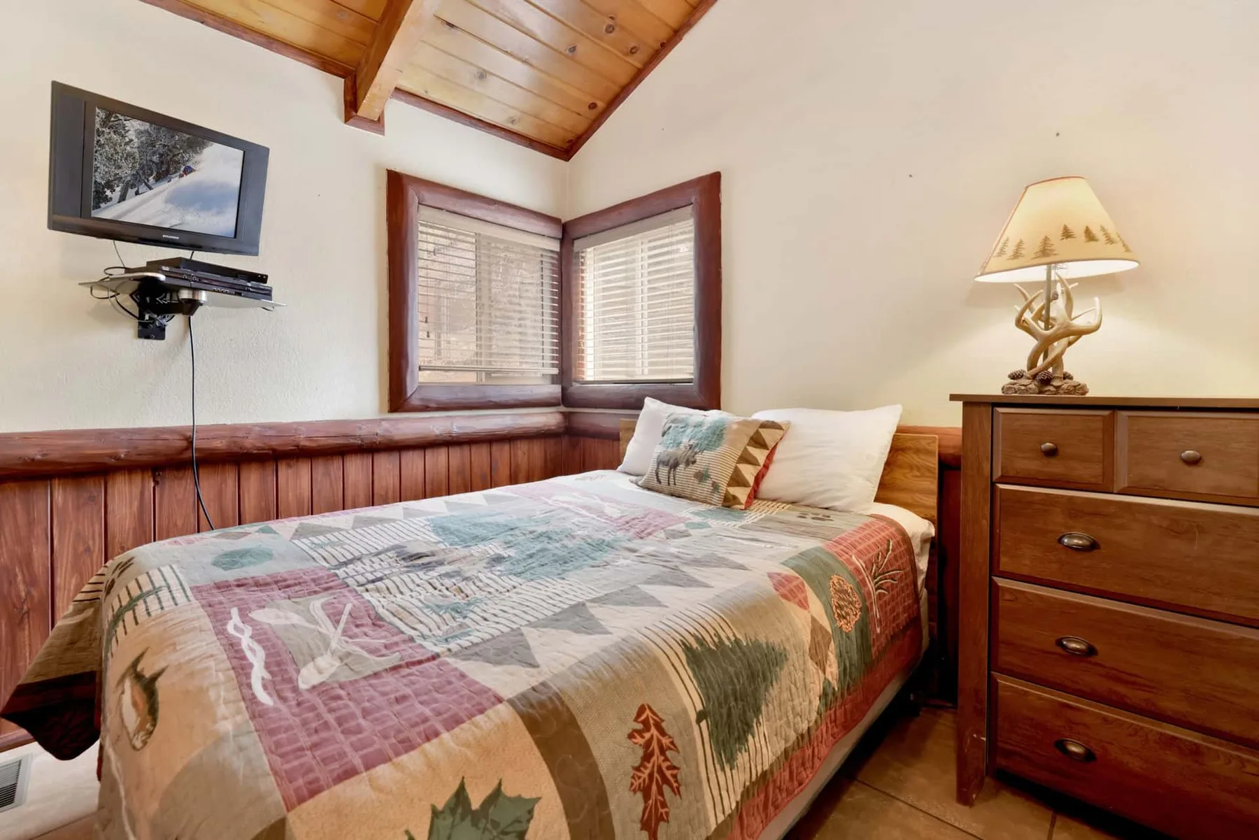 A bedroom with a bed beneath two windows and a wooden dresser.
