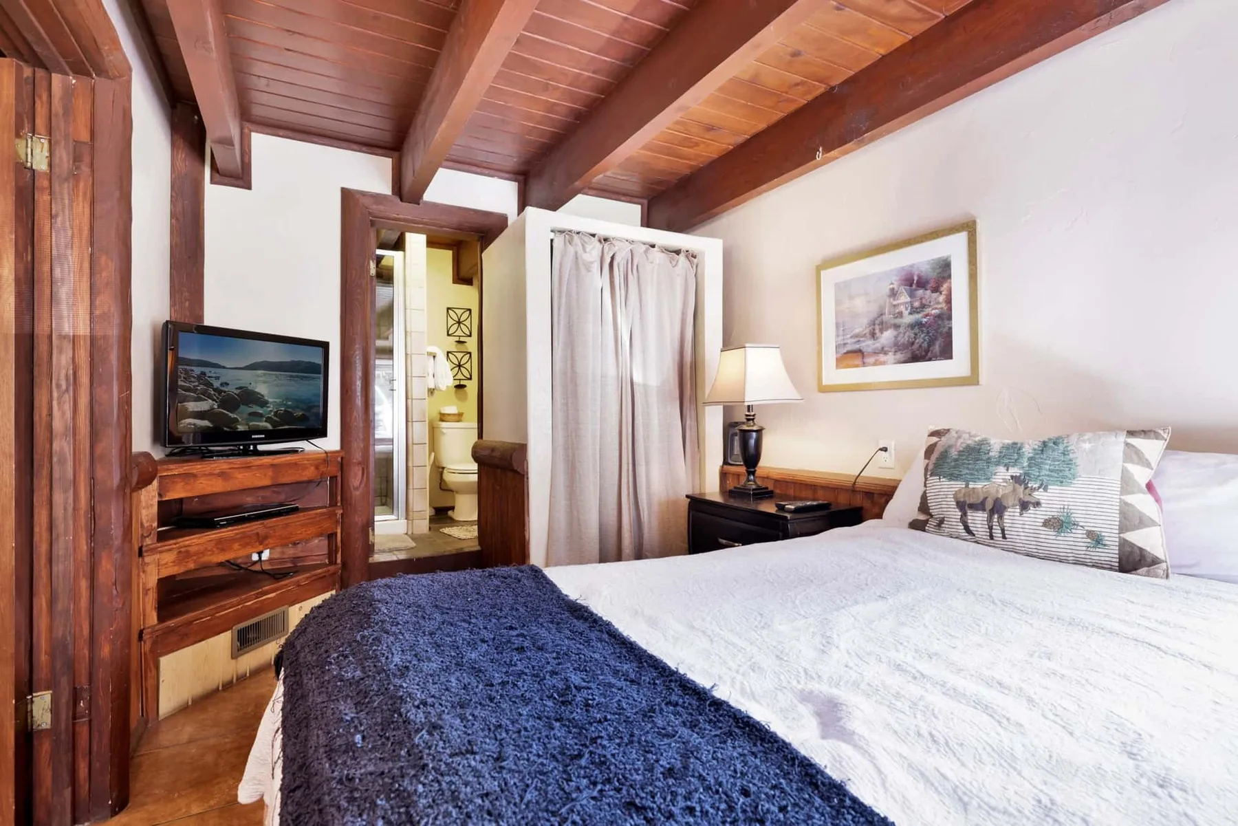 A bedroom with a bed, television, and exposed wooden ceiling beams.