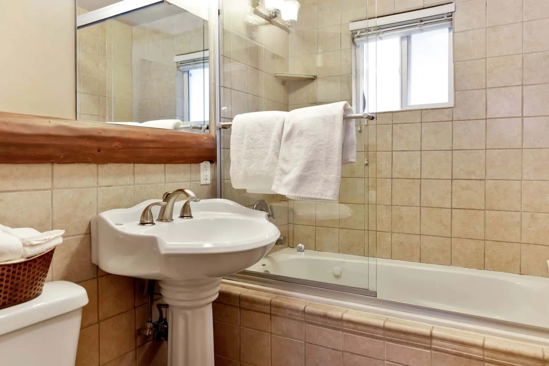 A tiled bathroom with a pedestal sink and bathtub.
