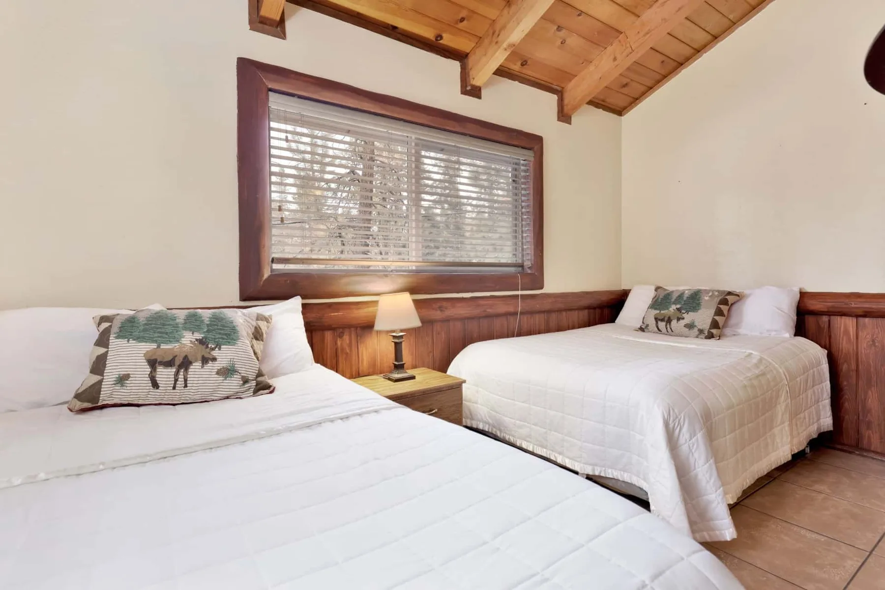 A bedroom with two beds, a bedside lamp, and a large window.