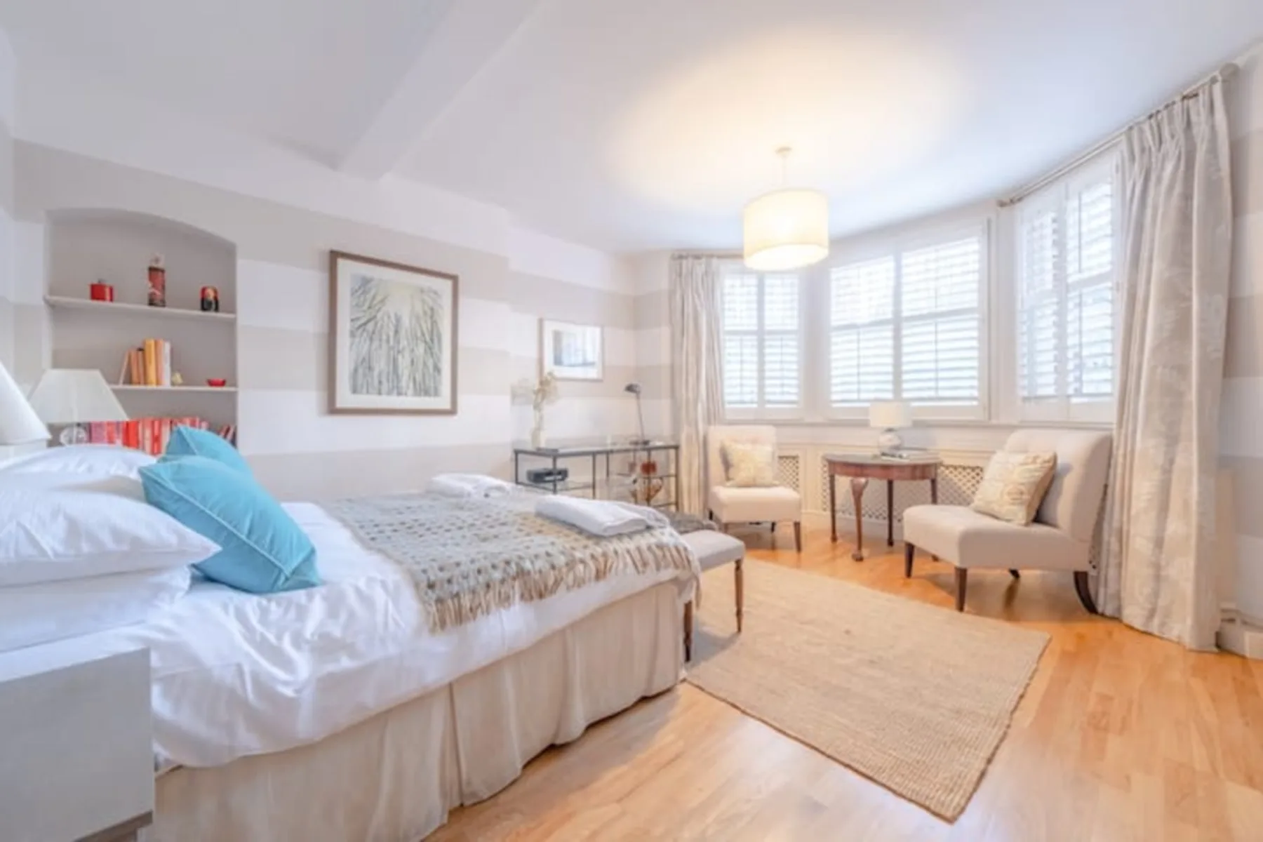 Dormitorio luminoso con una cama, asientos junto a la ventana y una mesa pequeña.