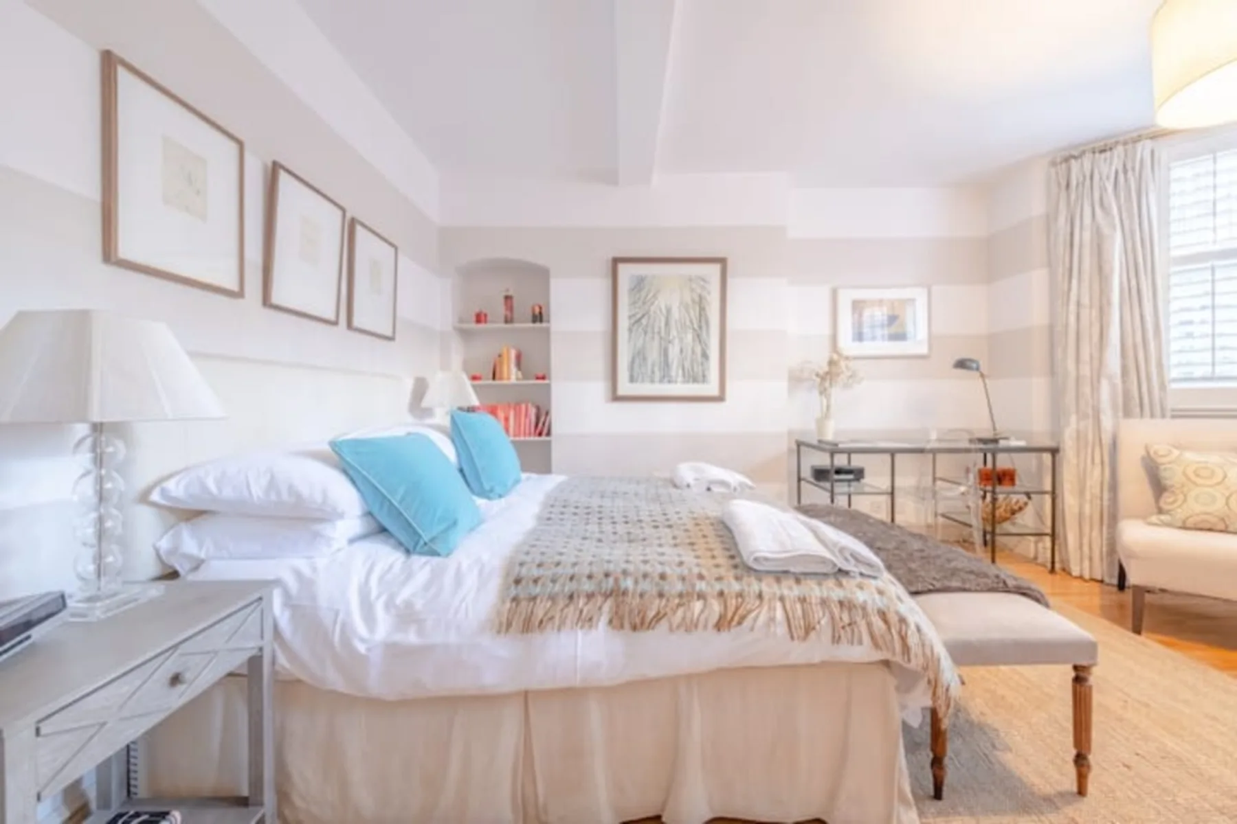 Un dormitorio luminoso con una cama bien tendida y cuadros enmarcados.
