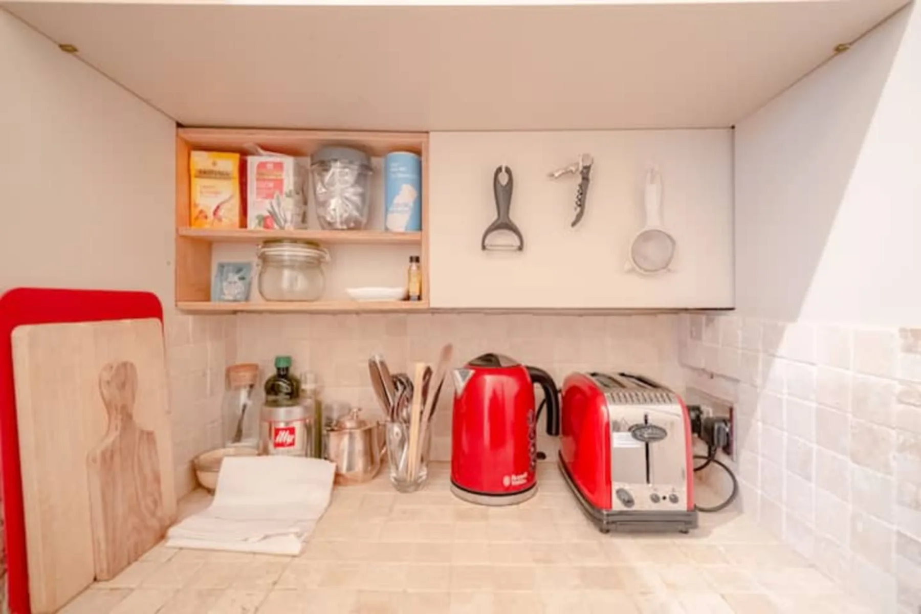 Una encimera de cocina con una tetera roja y una tostadora bajo armarios abiertos.