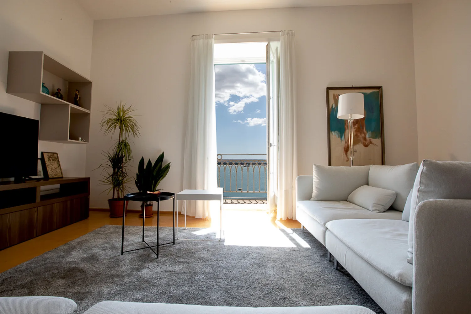 A bright living room with seating, a rug, and a window opening onto a balcony.