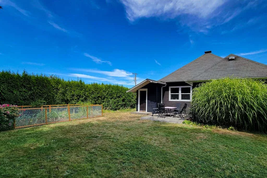 A house with a patio and outdoor seating stands beside a grassy yard.