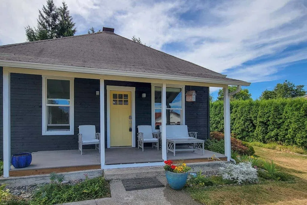 A small house with a covered porch, outdoor seating, and a garden.
