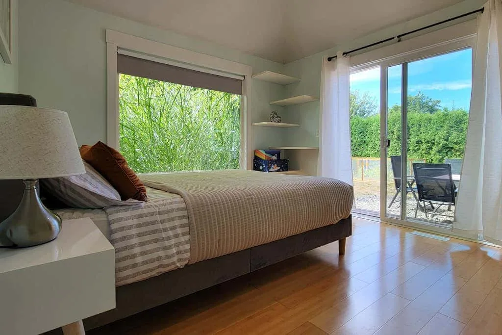 A bedroom with a bed beside a large window and sliding glass doors.