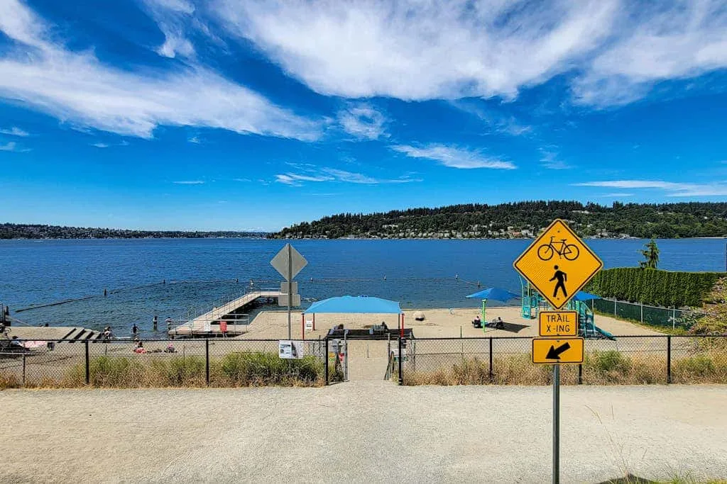 A lakeside beach and waterfront path sit beneath a bright blue sky.