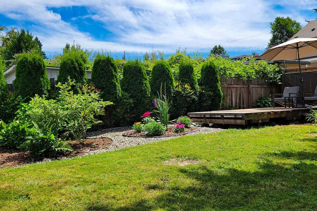 A garden patio with a wooden deck, outdoor seating, and a green lawn.