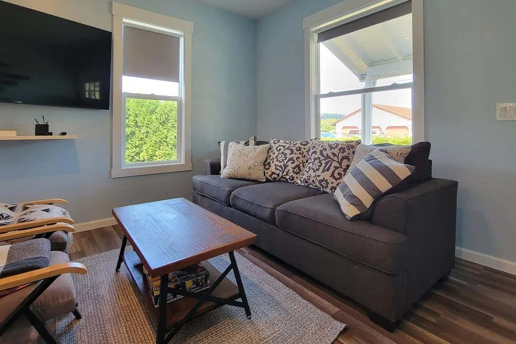 A living room with a dark sofa, patterned cushions, and a wooden coffee table.