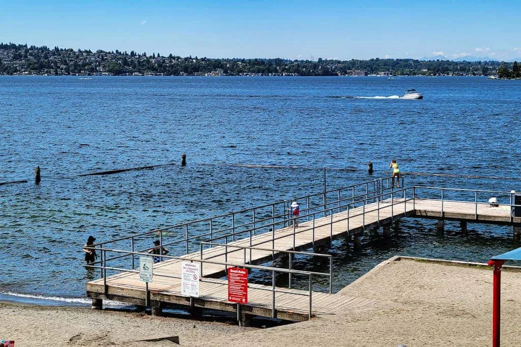 A wooden pier extends over the water beside a sandy beach.