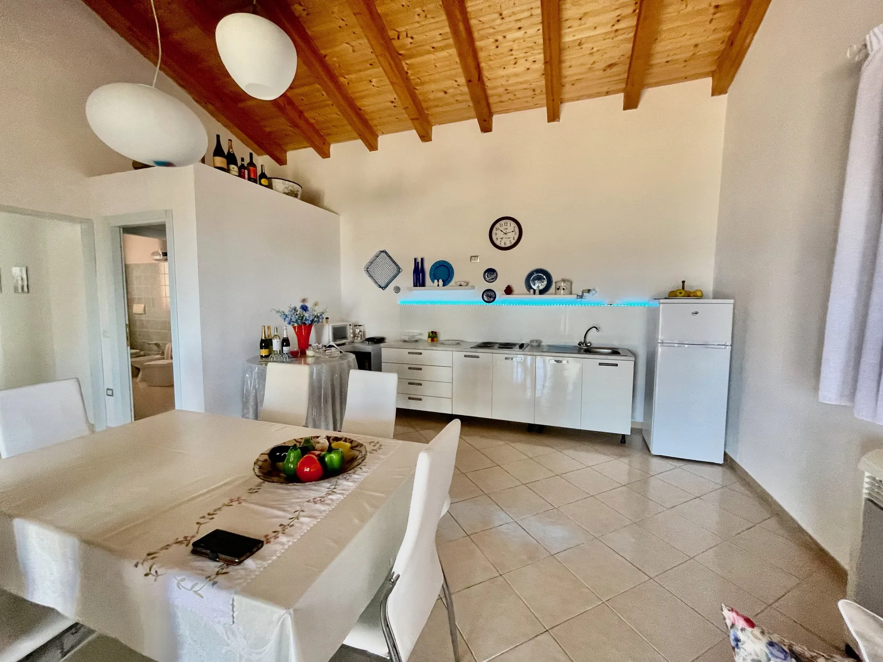 Comedor y cocina con una mesa, gabinetes blancos y un techo inclinado de madera.