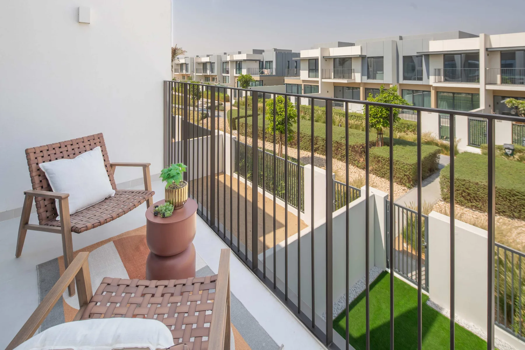 A balcony with seating overlooks landscaped paths and modern residential buildings.