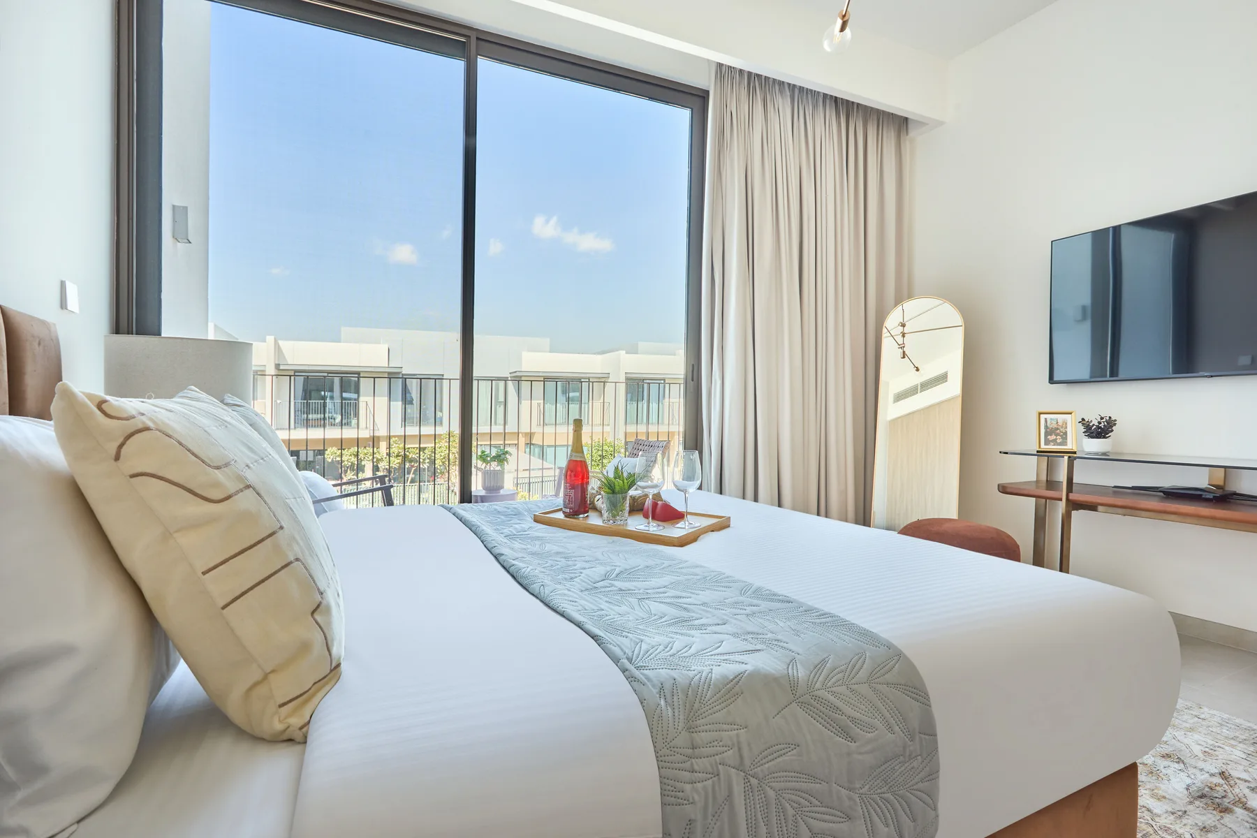 A bright bedroom with a neatly made bed beside large windows and a television.