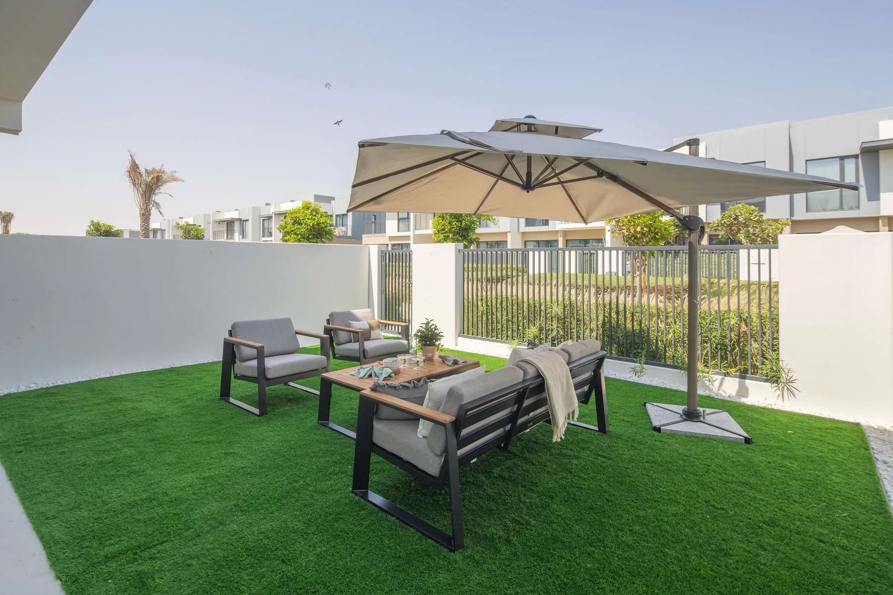 An outdoor seating area on green turf sits beneath a large patio umbrella.