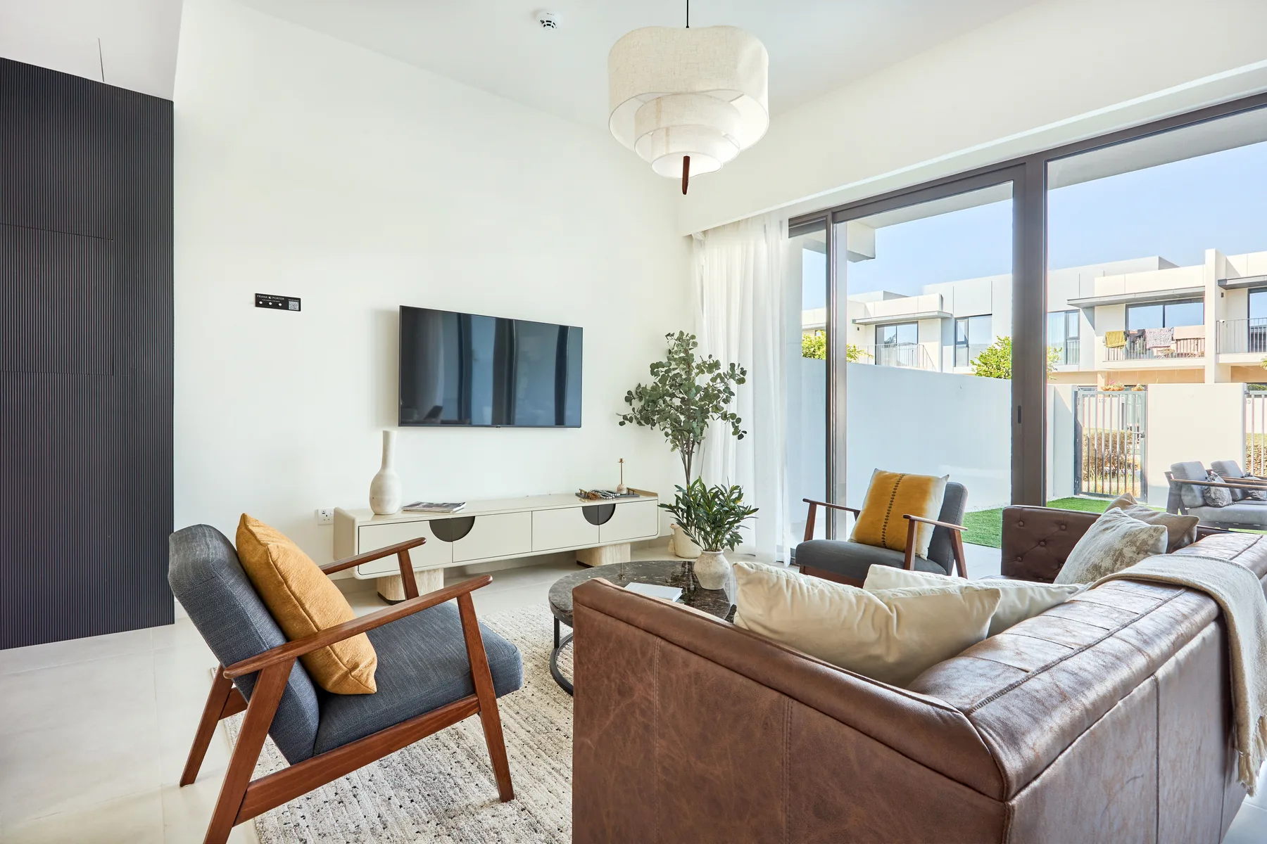 Una sala luminosa con asientos, un televisor y grandes ventanas.