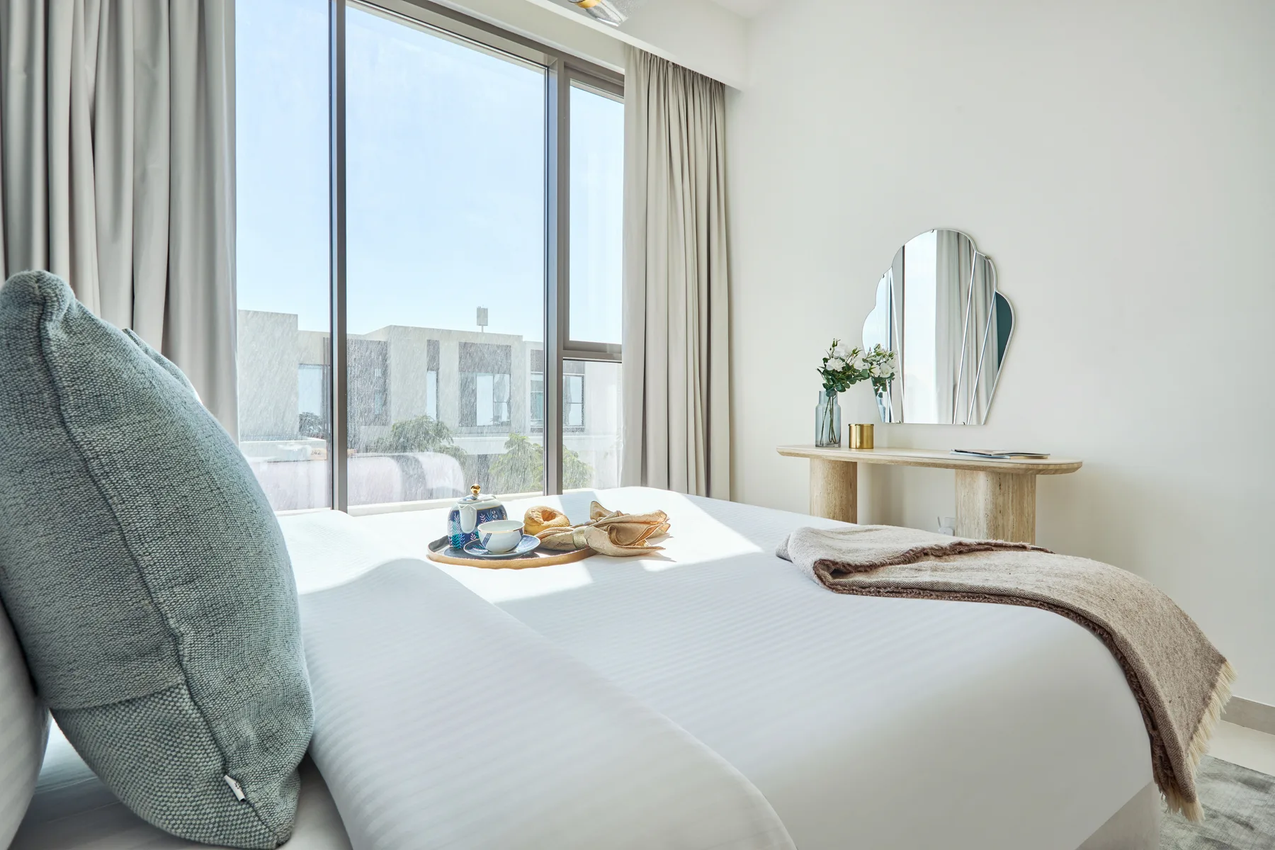 A bright bedroom with a neatly made bed beside a large window.