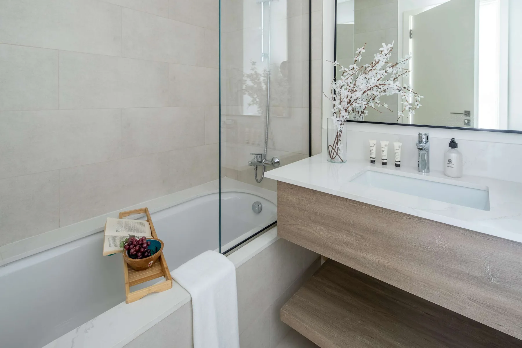 A bright bathroom with a bathtub, glass shower screen, and wide vanity.