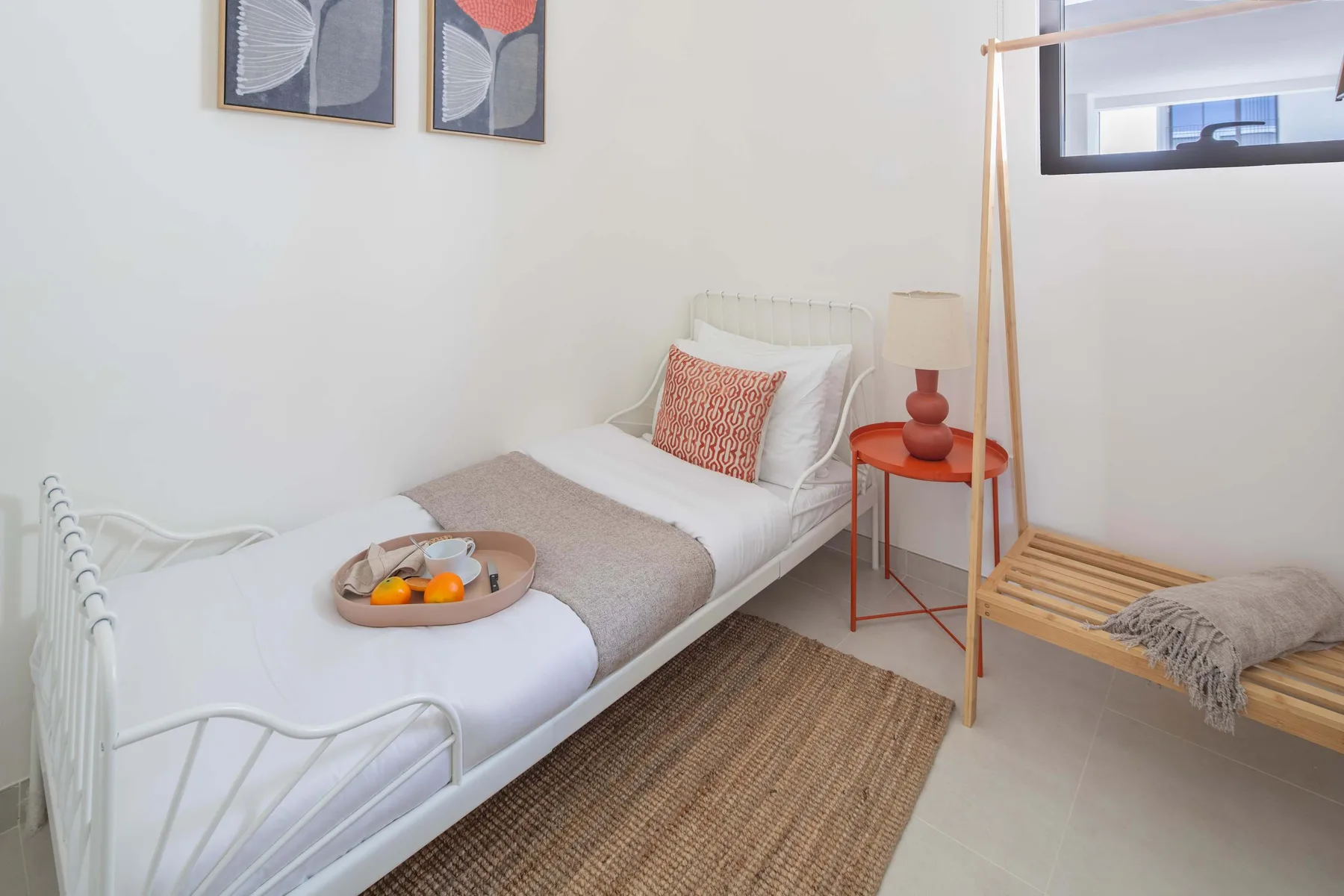 A bedroom with a single bed, a bedside table, and a wooden bench.