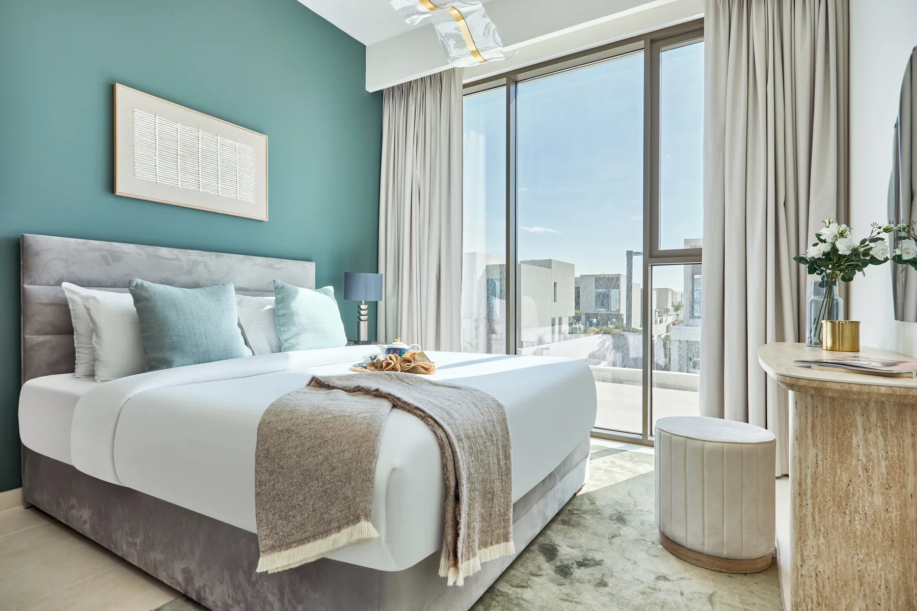 A bright bedroom with a neatly made bed beside large windows.