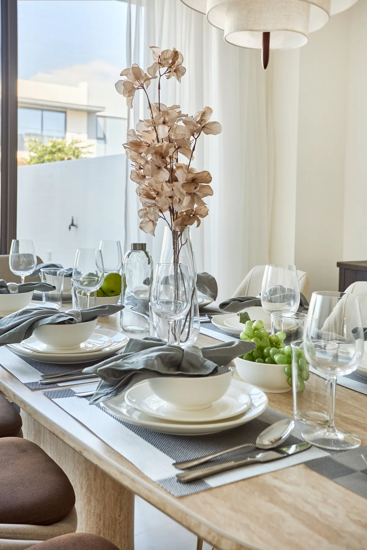 A dining table is set with plates, glassware, and a dried floral centerpiece.