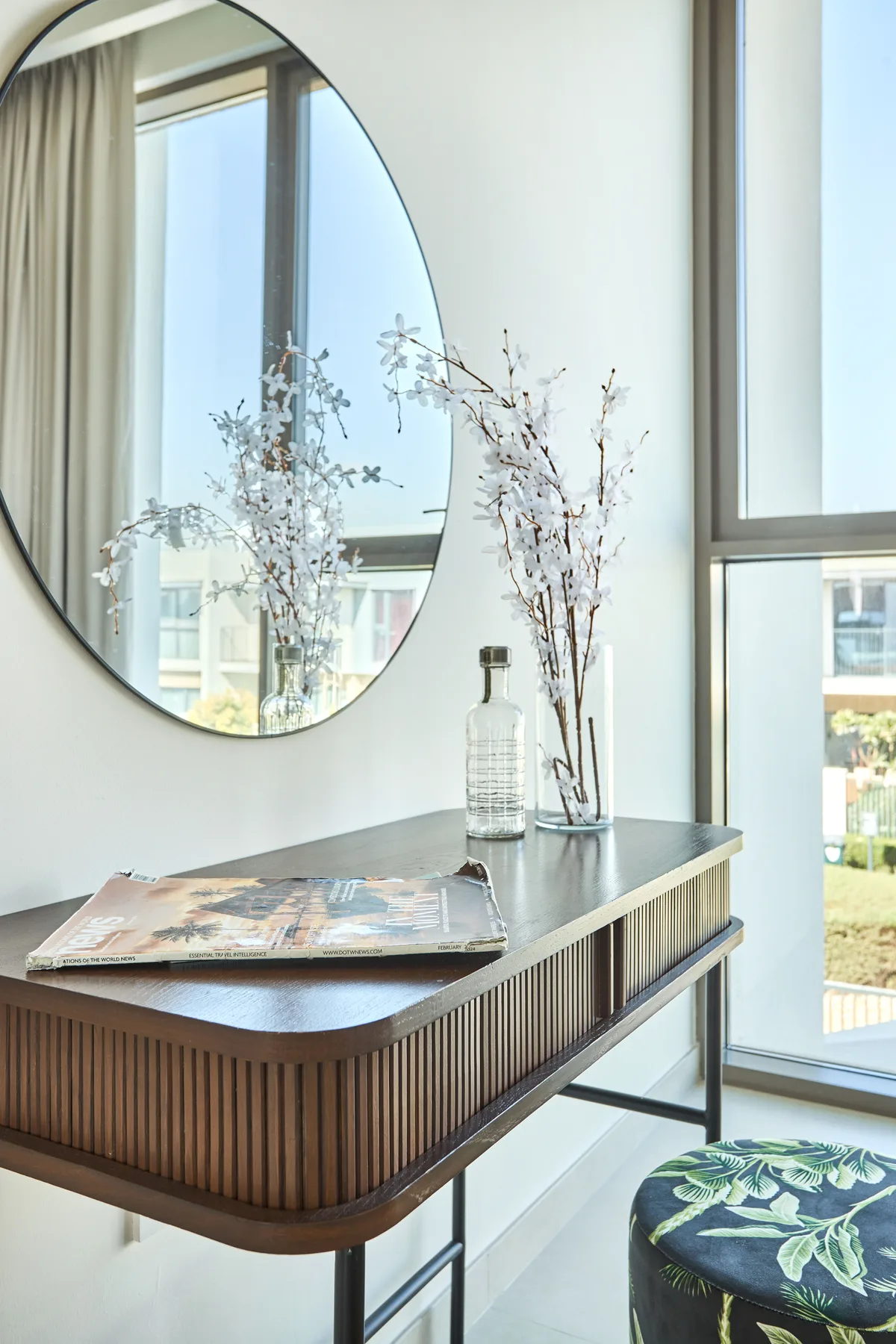 A bright sitting area with a rounded wooden console beneath a large mirror.