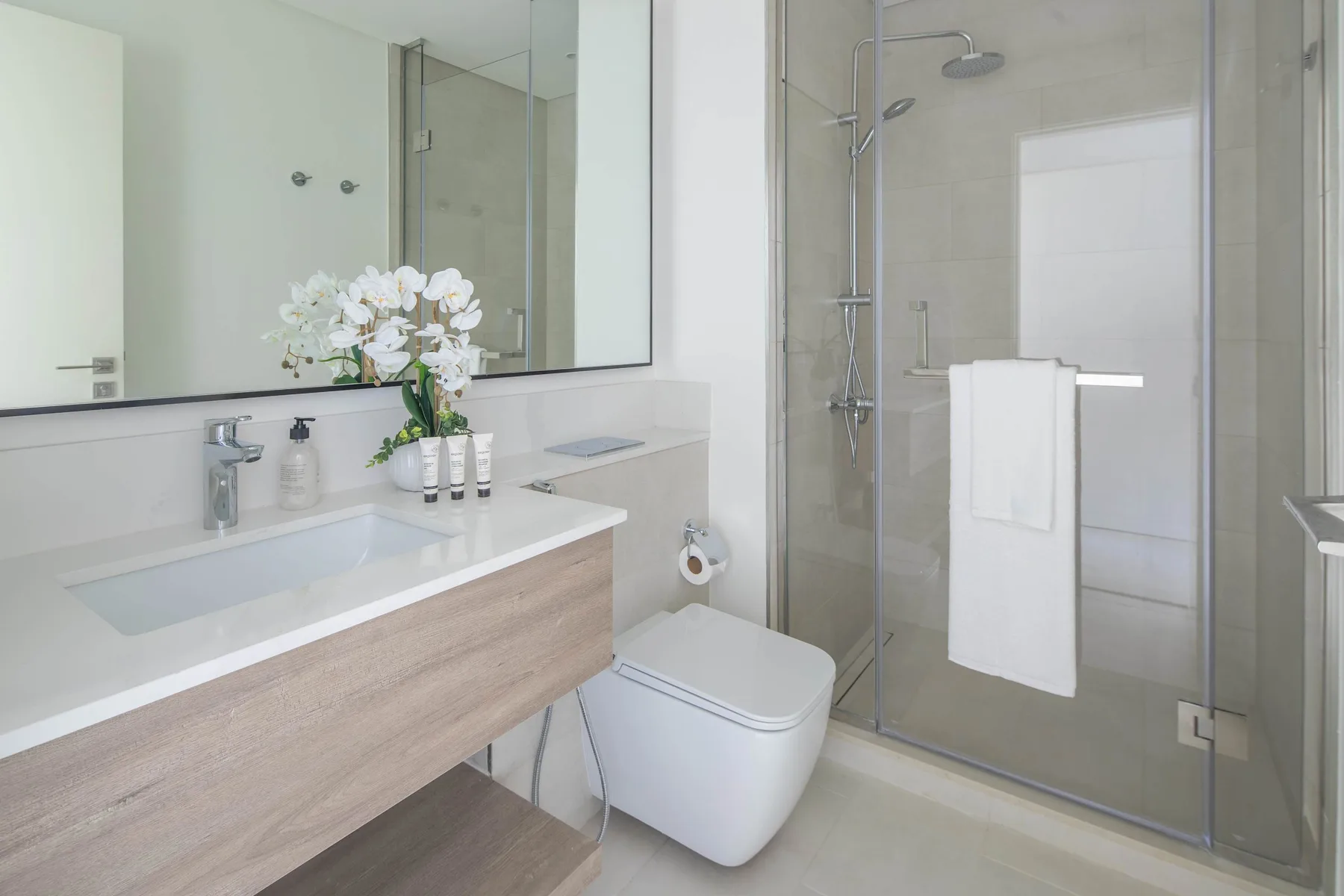 A bright bathroom with a sink vanity, toilet, and glass-enclosed shower.