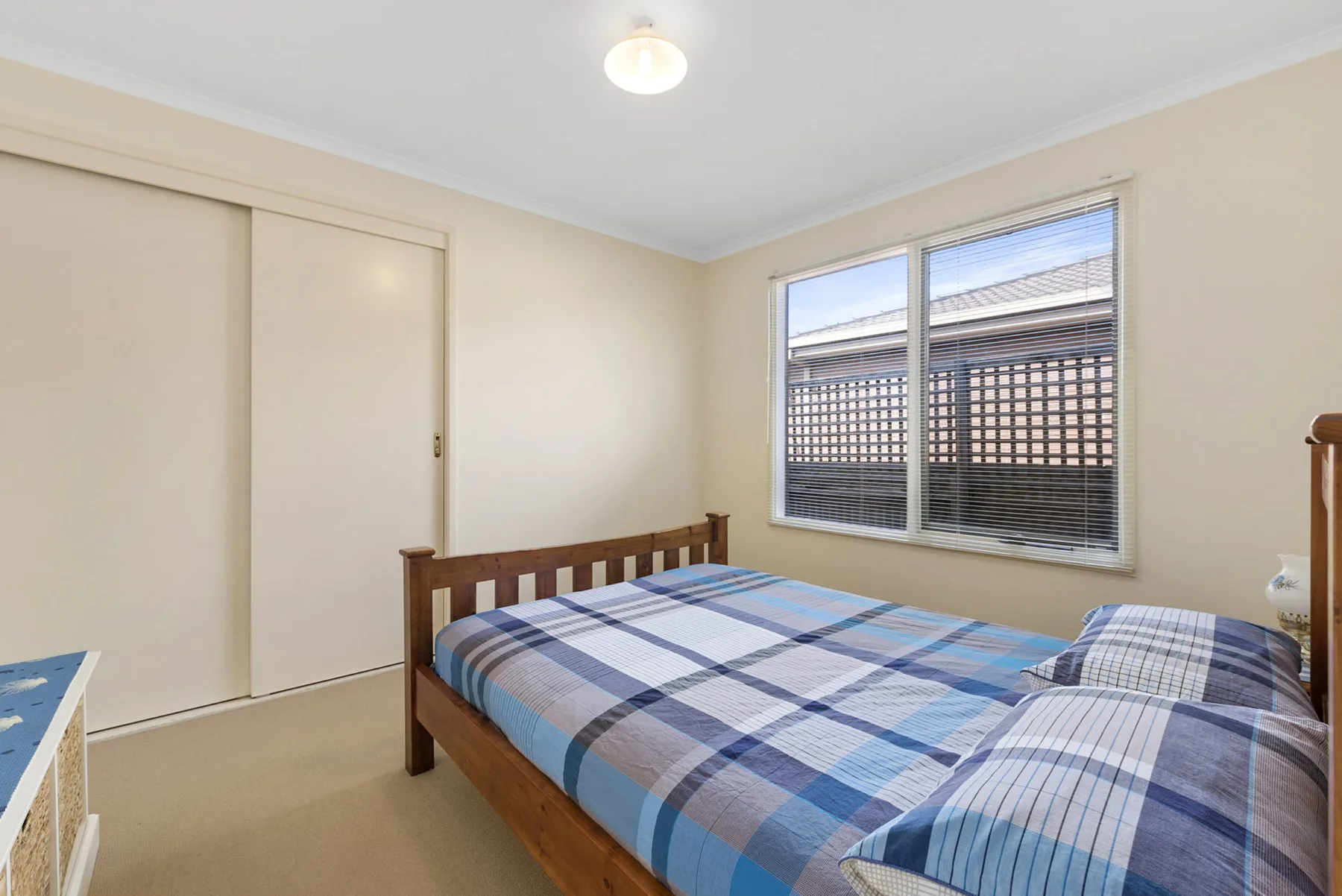 A bedroom with a wooden bed dressed in blue plaid bedding beside a window.