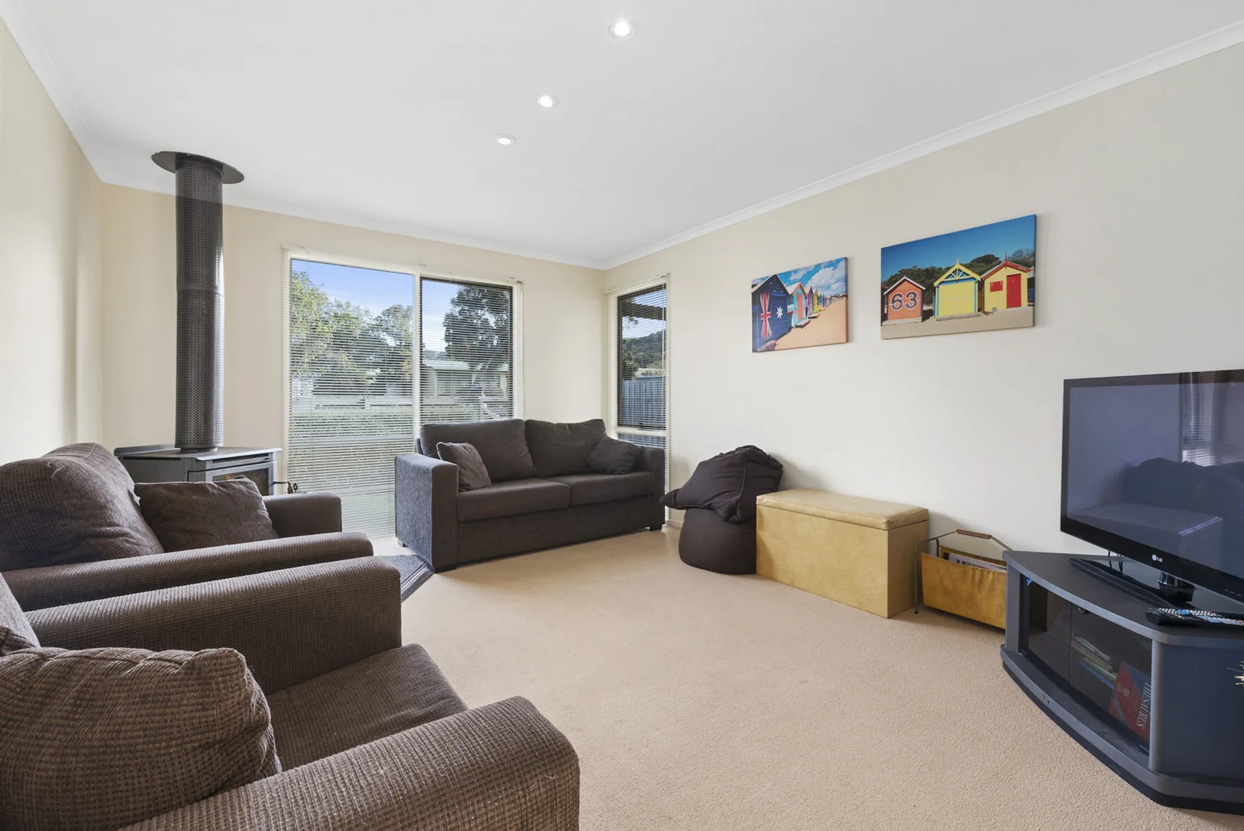 A living room with seating, a television, and windows overlooking greenery.
