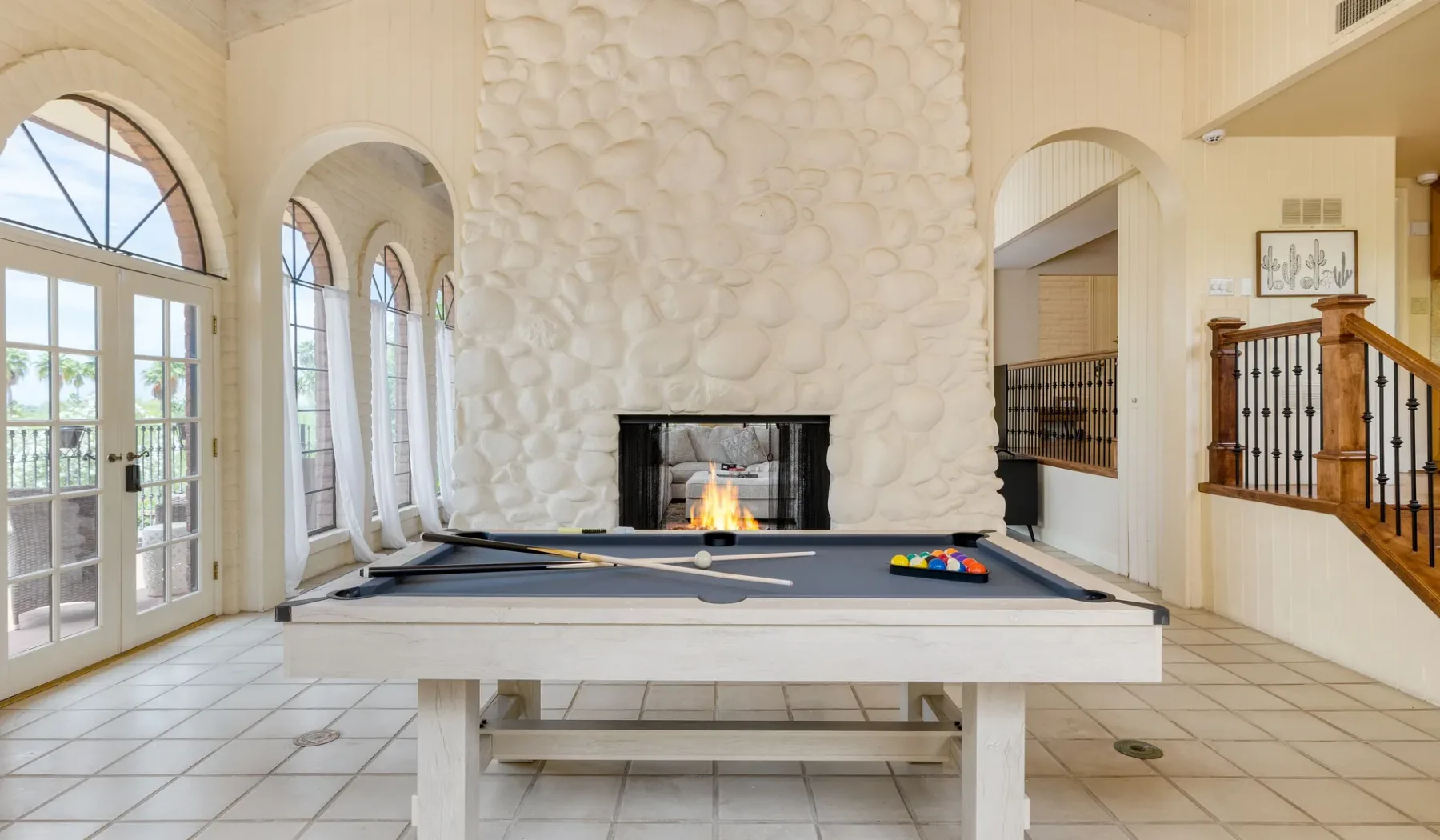 Una amplia sala de juegos tiene una mesa de billar frente a una chimenea de piedra.