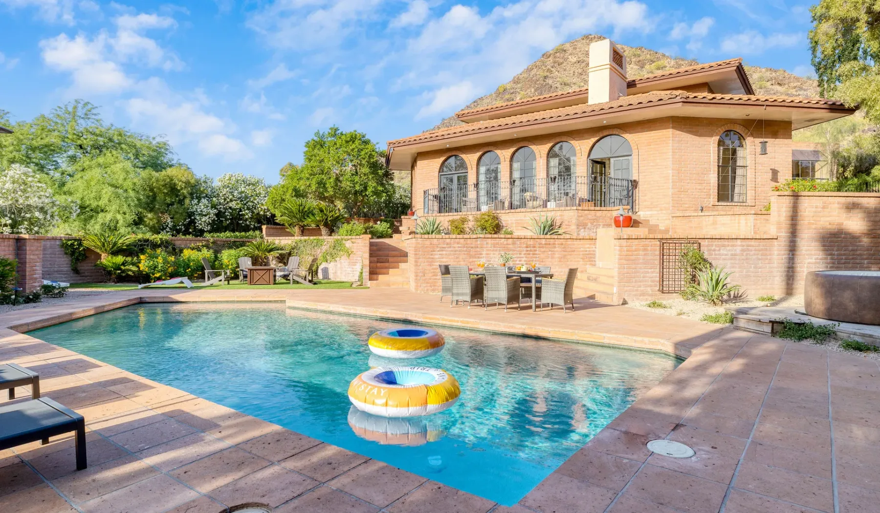 Una piscina junto a una casa de ladrillo, con flotadores coloridos en el agua.