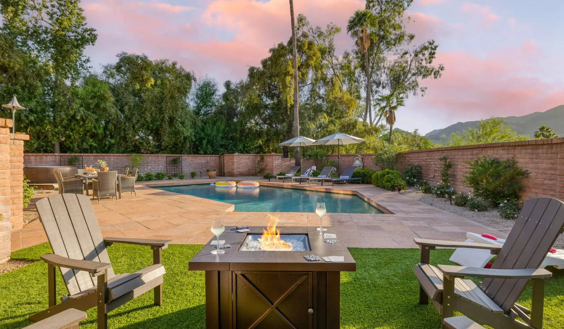 Un patio exterior da a una piscina, con asientos y una mesa con fuego.