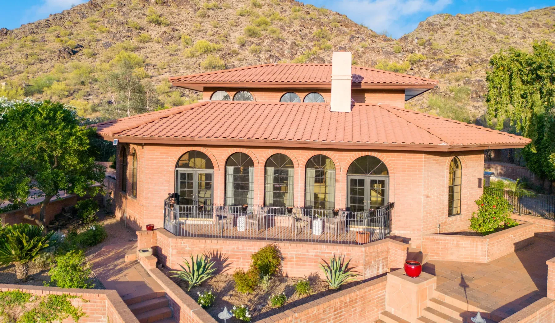 Una casa de ladrillo con ventanas arqueadas y techo de terracota está frente a una ladera.