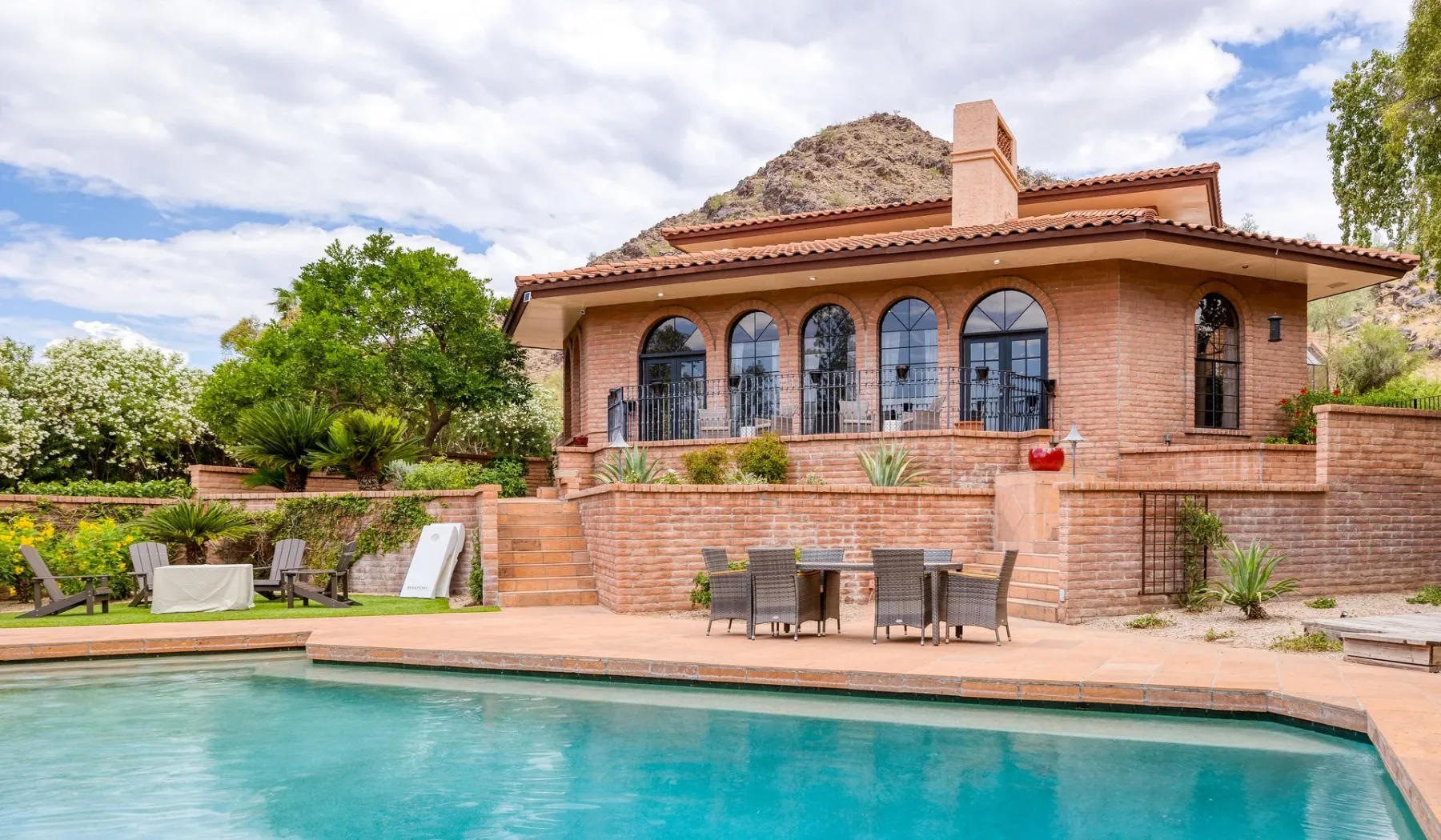 Una casa de ladrillo da a una piscina, con asientos al aire libre junto al agua.